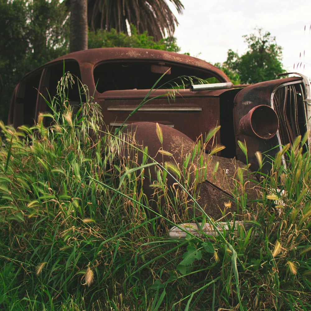 an old rusted car sitting in a field of tall grass
