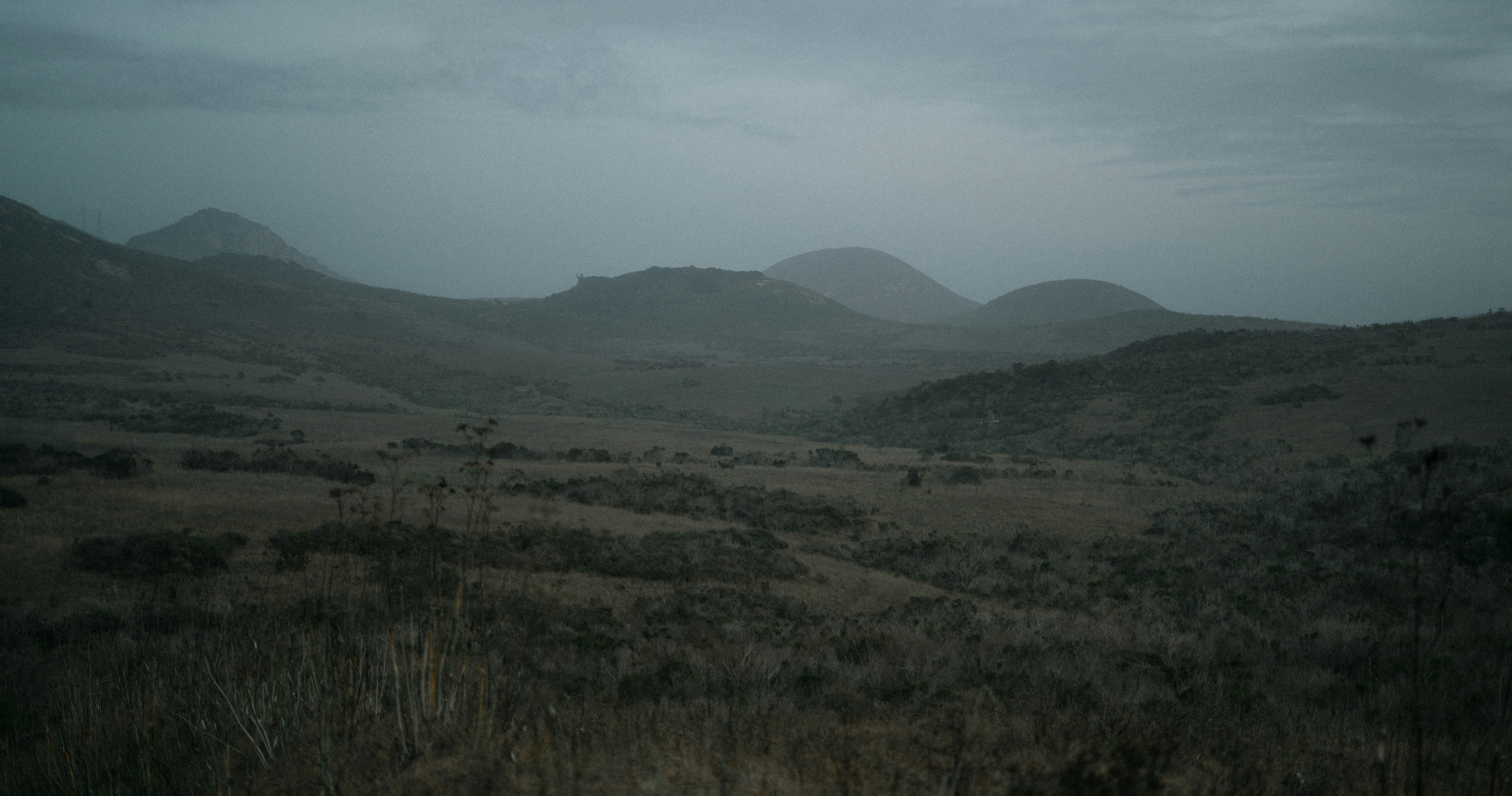 a field with hills in the distance under a cloudy sky