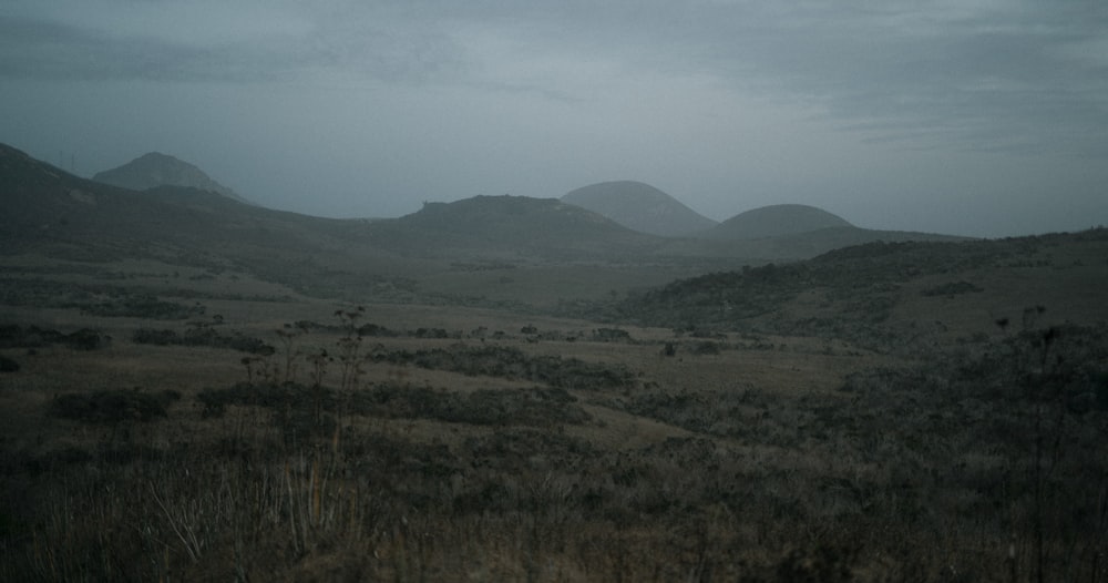 a field with hills in the distance under a cloudy sky