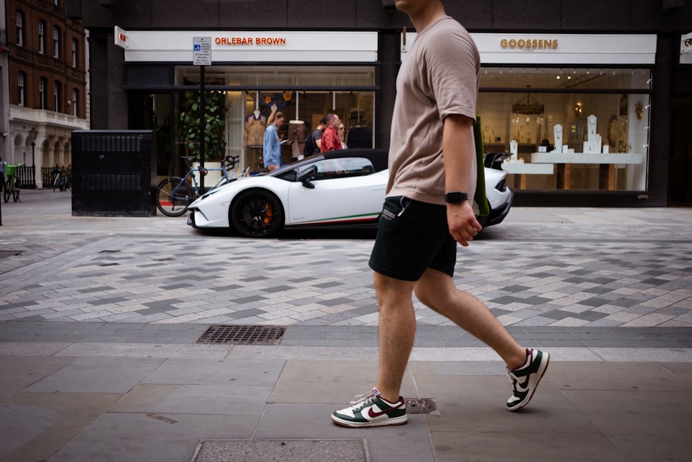 a man walking down a street next to a white sports car