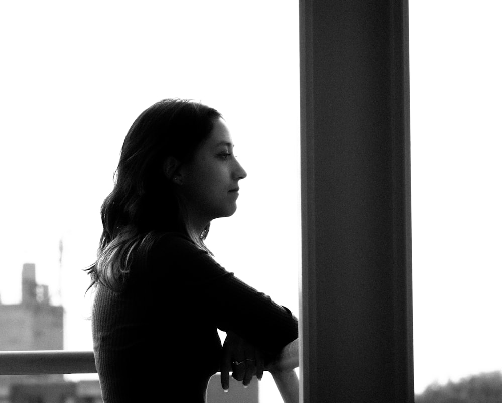 a black and white photo of a woman looking out a window