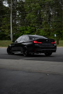 a black car driving down a street next to a forest