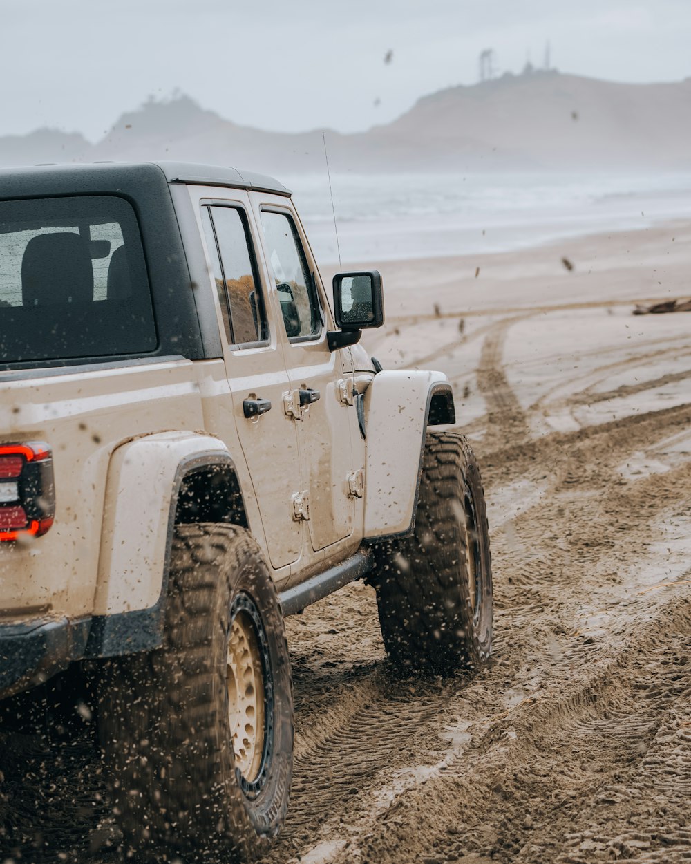 a white jeep driving down a dirt road next to the ocean