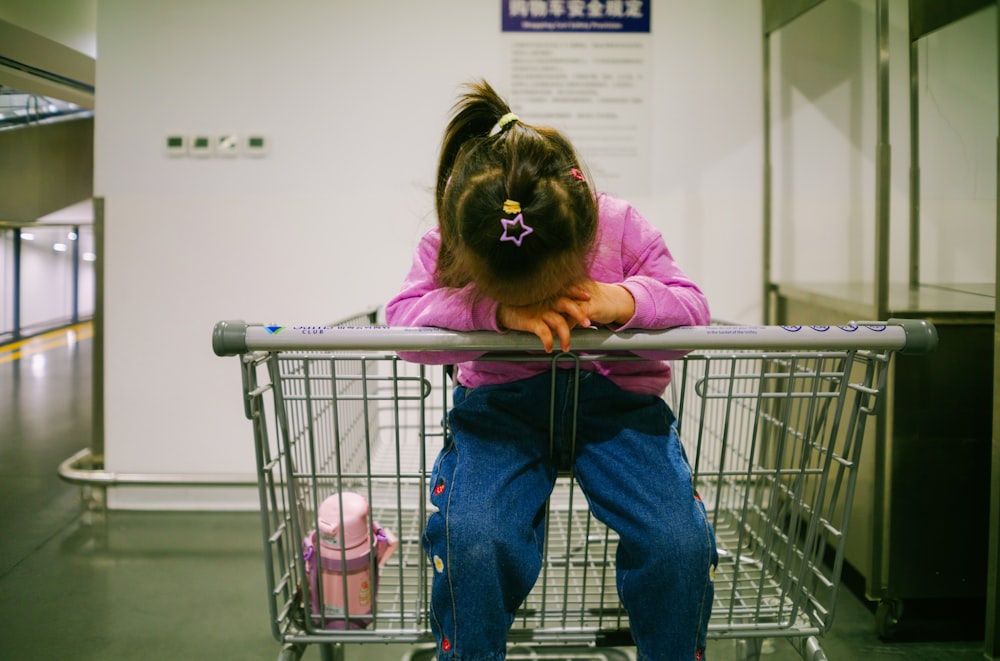 a little girl sitting on top of a shopping cart