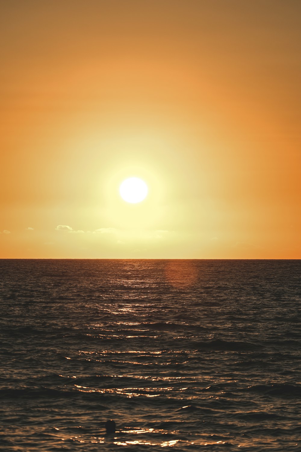 the sun is setting over the ocean with a person in the water