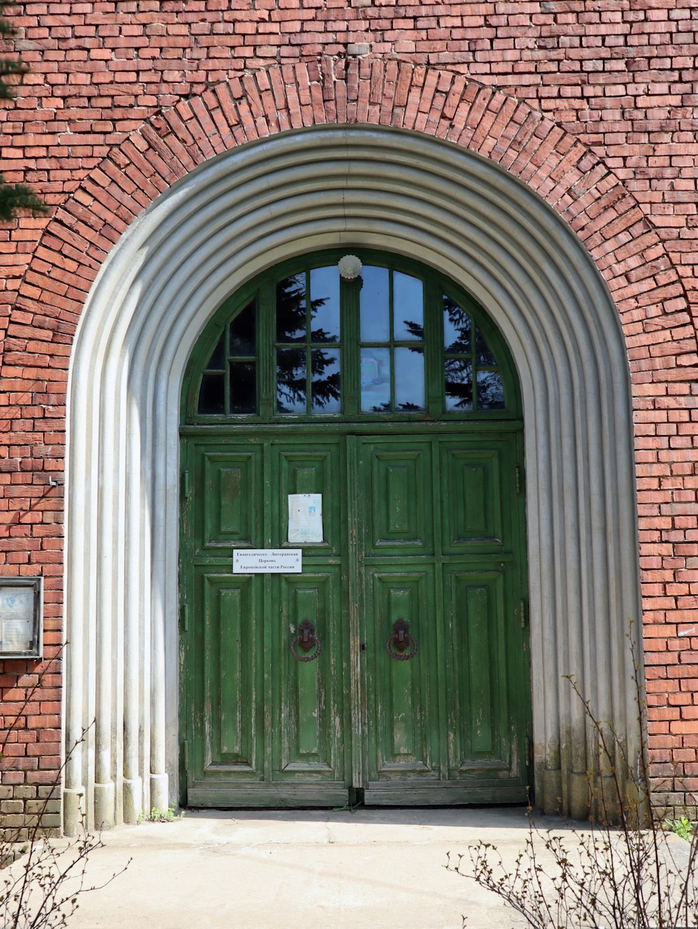 a large green door with arched windows on a brick building
