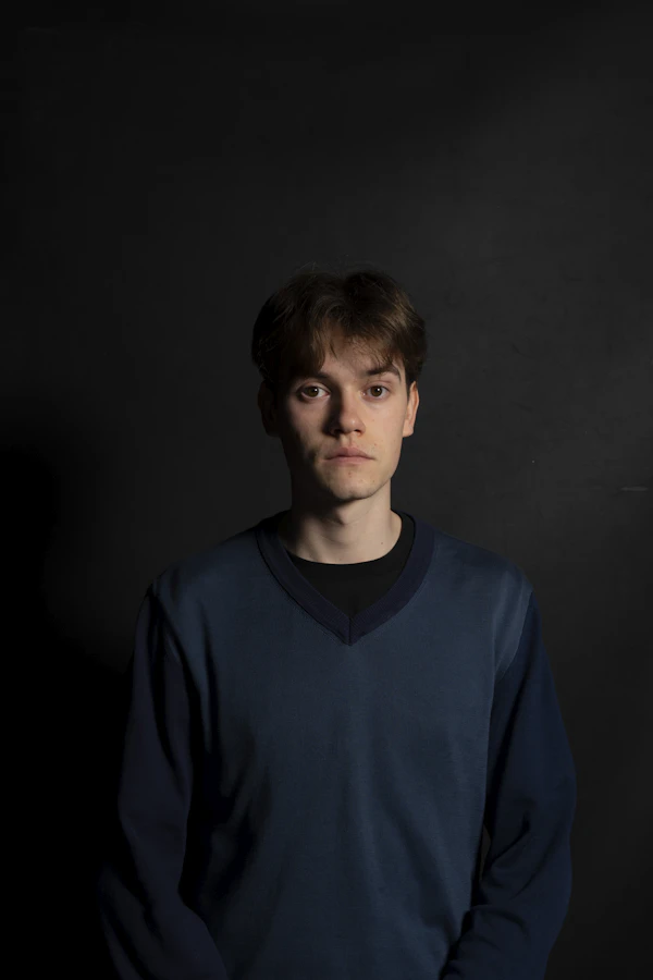 Portrait d'un homme debout devant un fond noir.