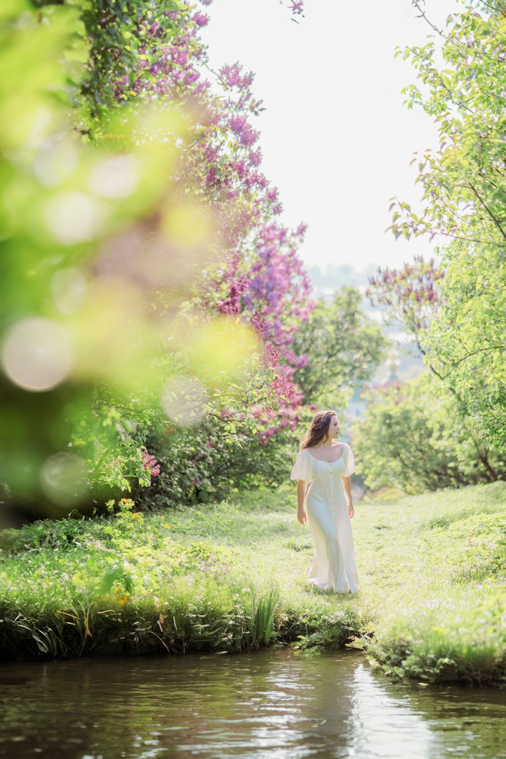 a woman in a white dress standing by a river