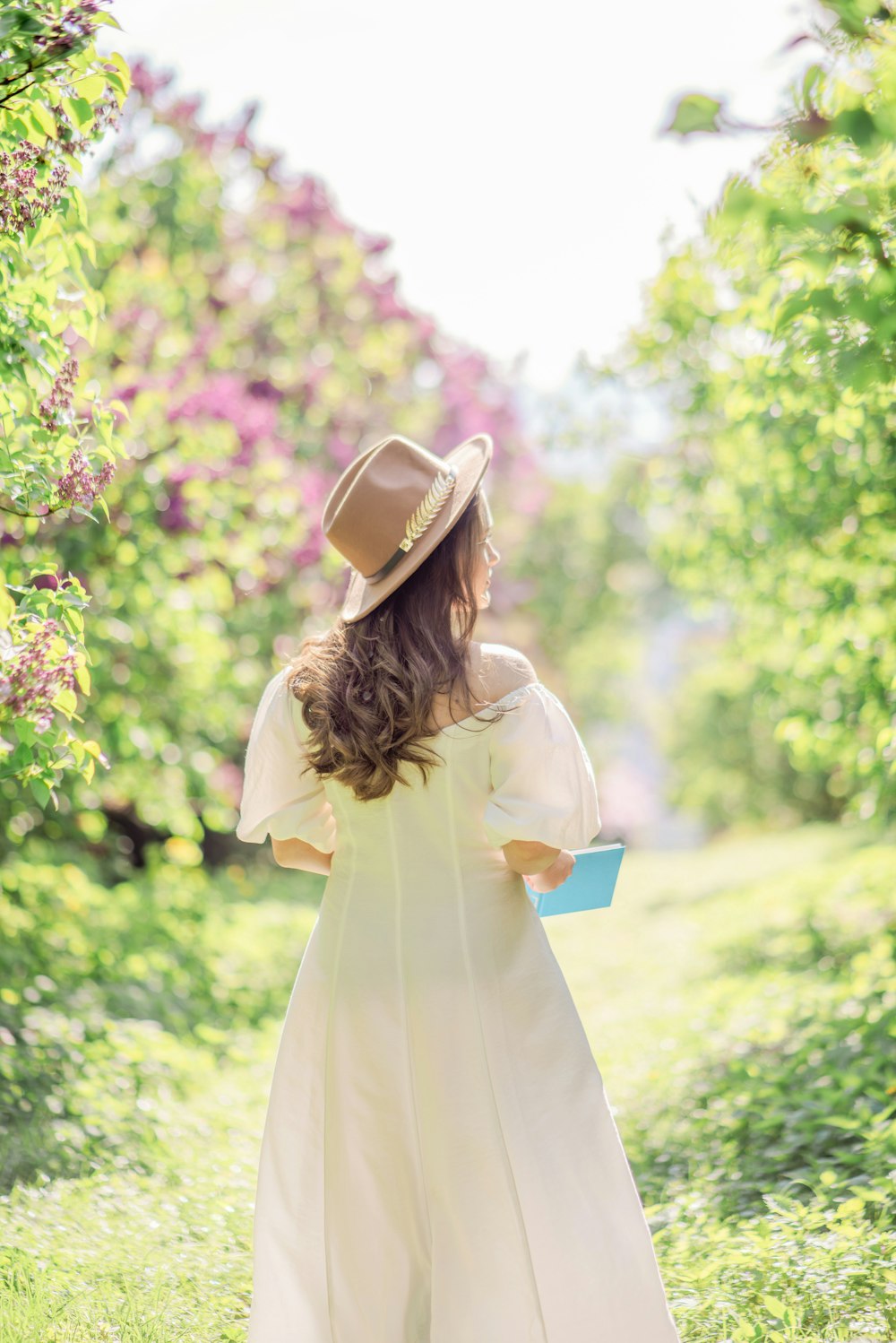 a woman in a white dress and hat walking through a field