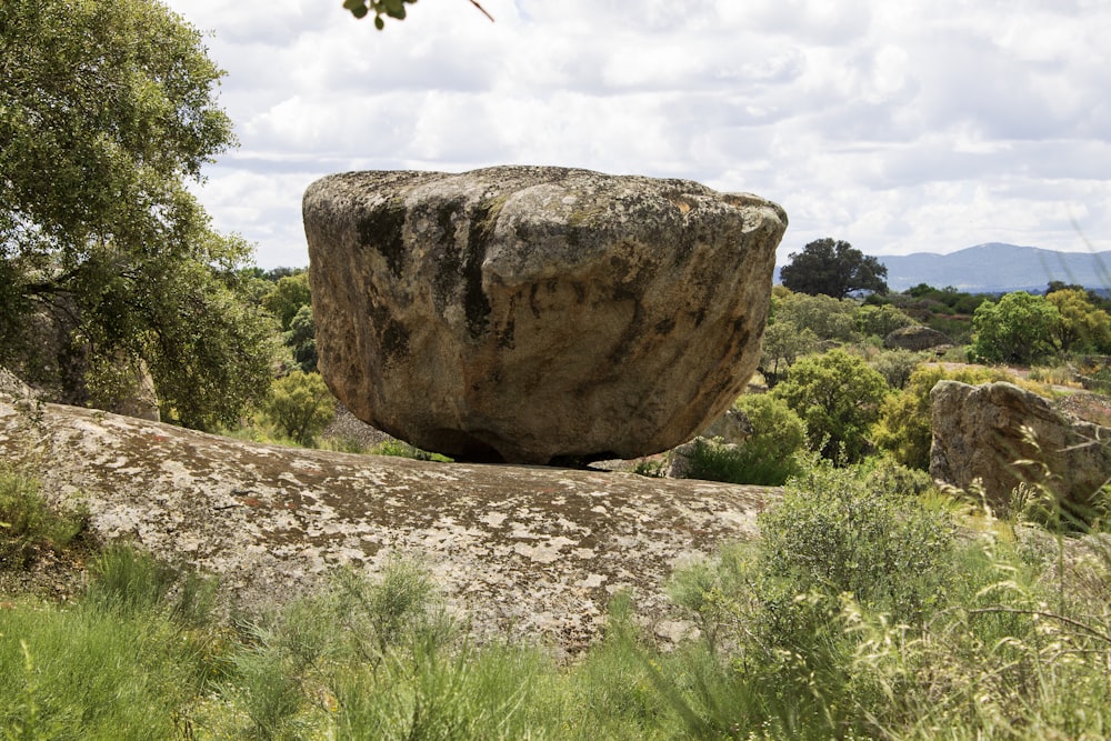 a large rock sitting in the middle of a lush green field