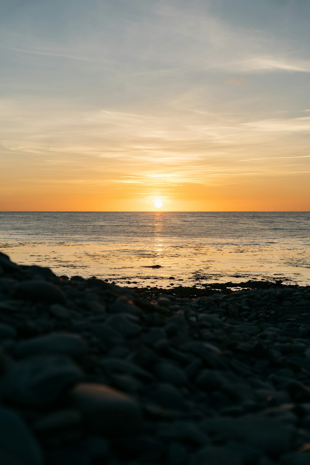 the sun is setting over the ocean on a rocky beach