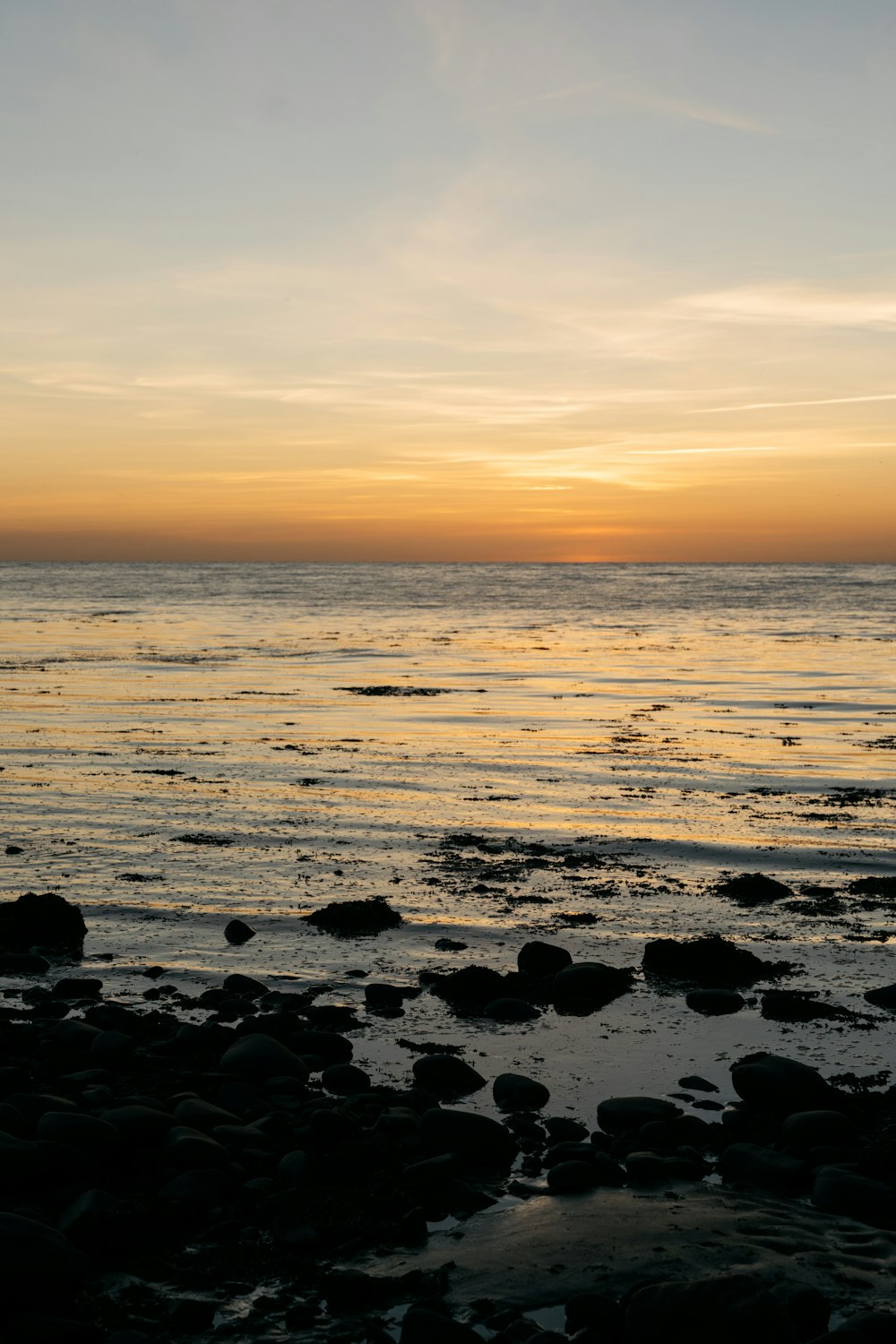 the sun is setting over the ocean with rocks in the foreground