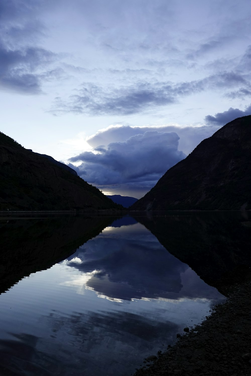 a body of water surrounded by mountains under a cloudy sky