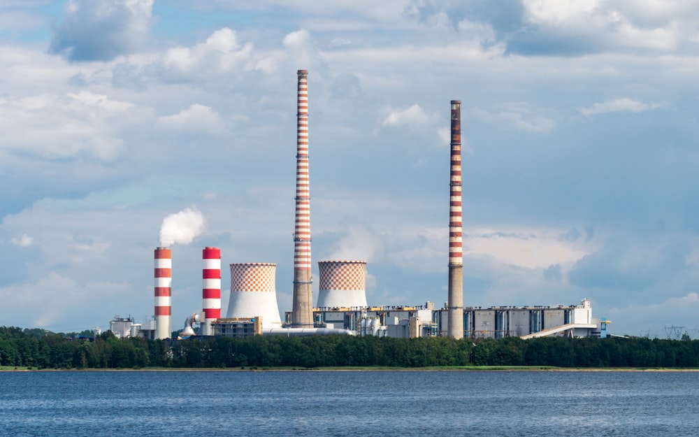 smoke stacks rise from a factory near a body of water