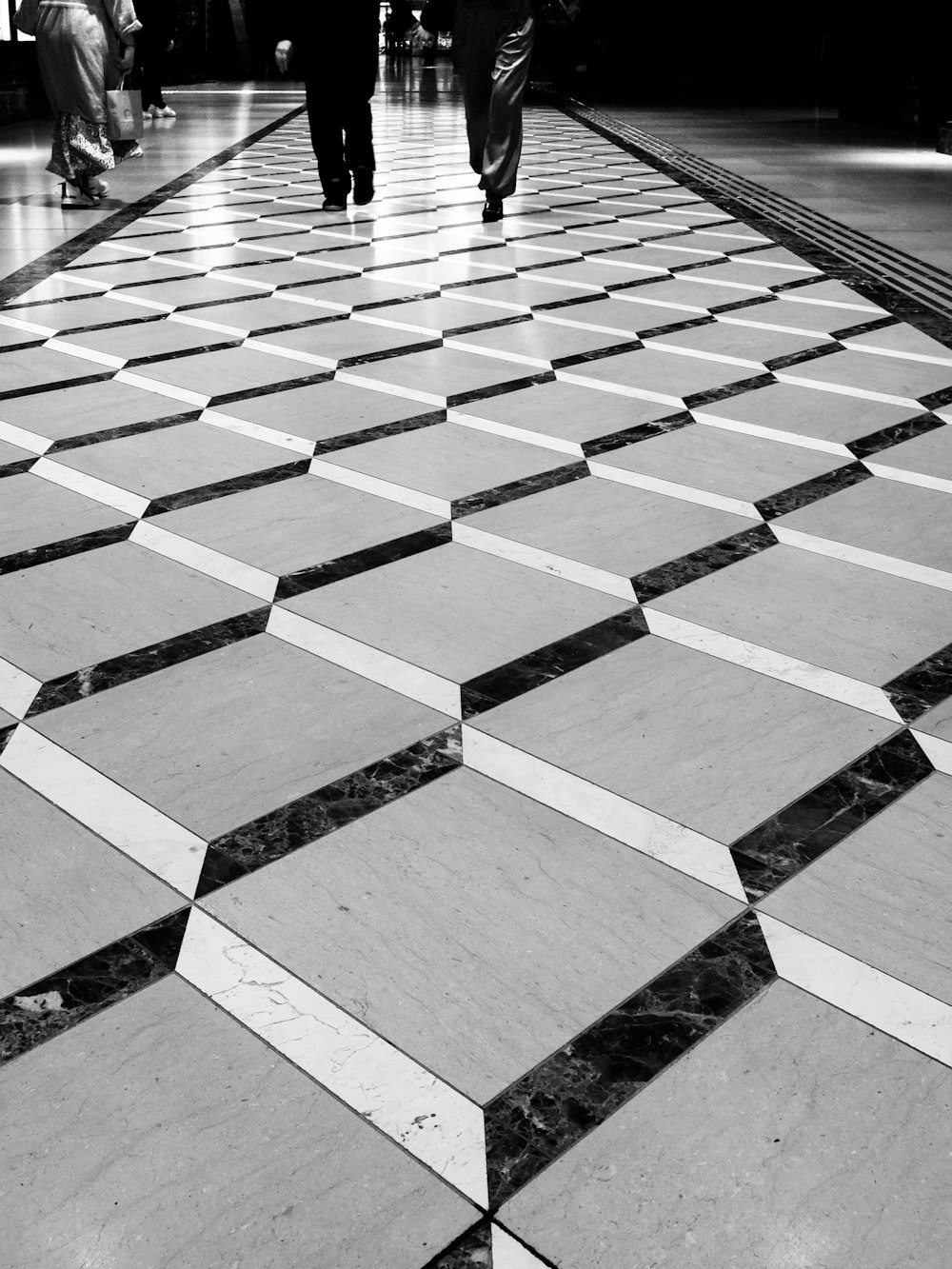 a black and white photo of people walking down a tiled floor