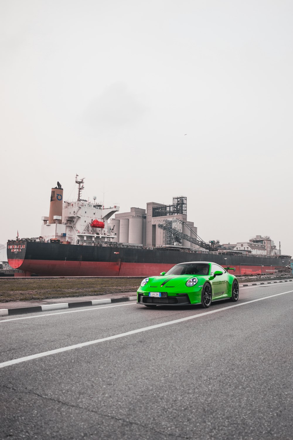 a green sports car driving down a road next to a large ship