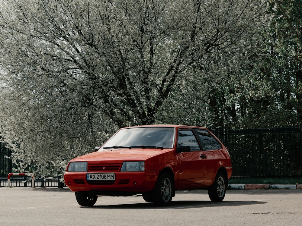 a red car parked in a parking lot next to a tree