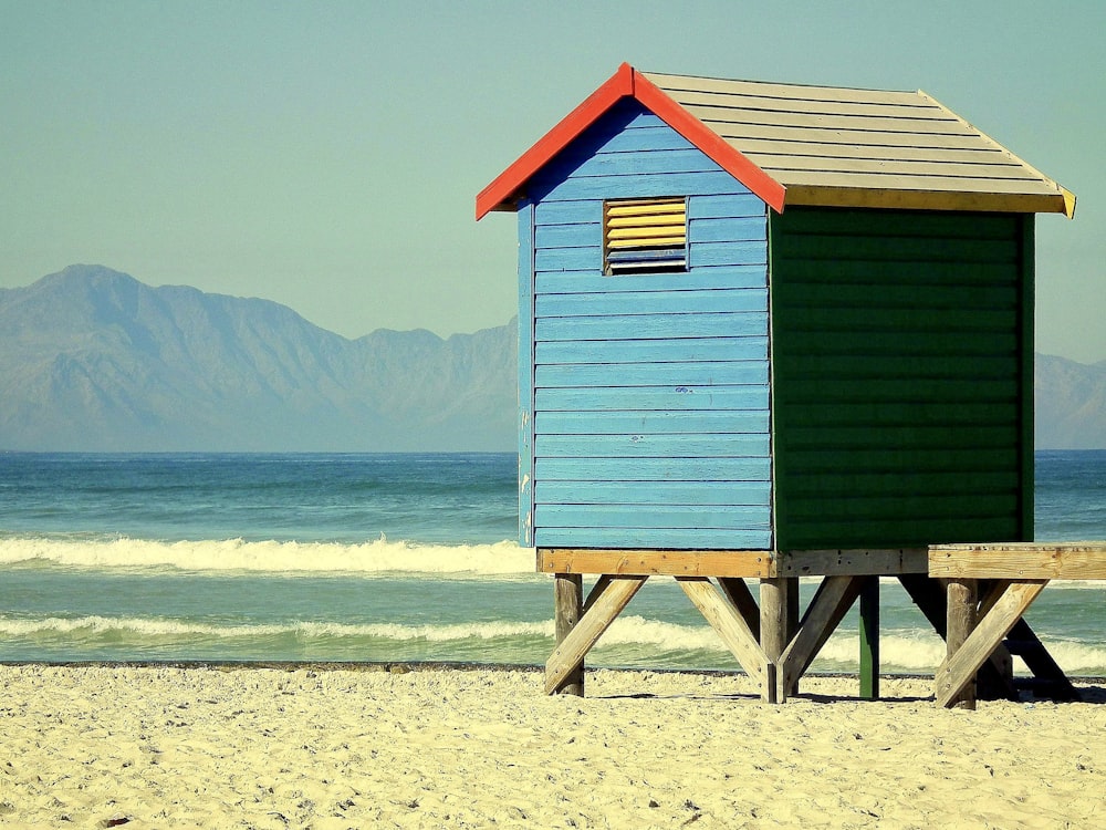 a small blue and green beach hut sitting on top of a sandy beach