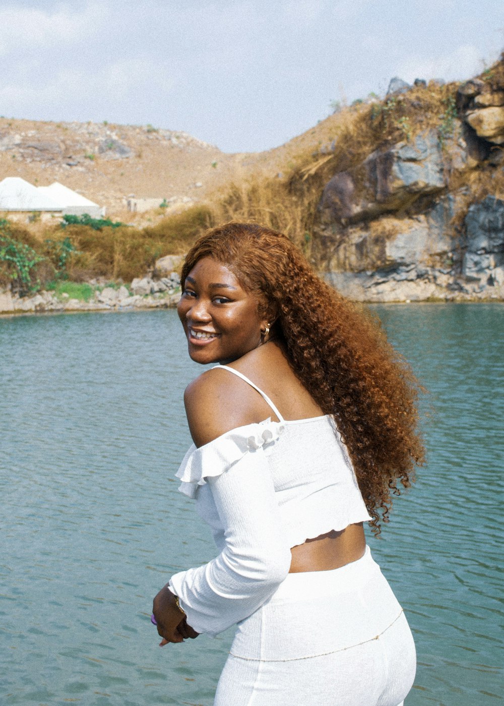 a woman in a white outfit standing in front of a body of water