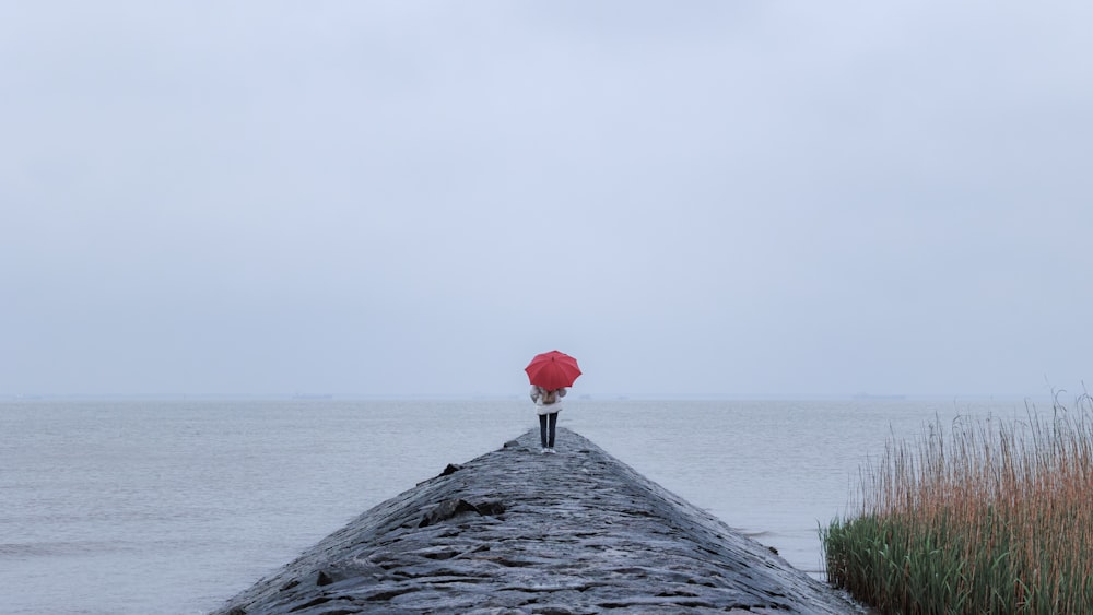 eine Person mit einem roten Regenschirm, die auf einem Pier steht