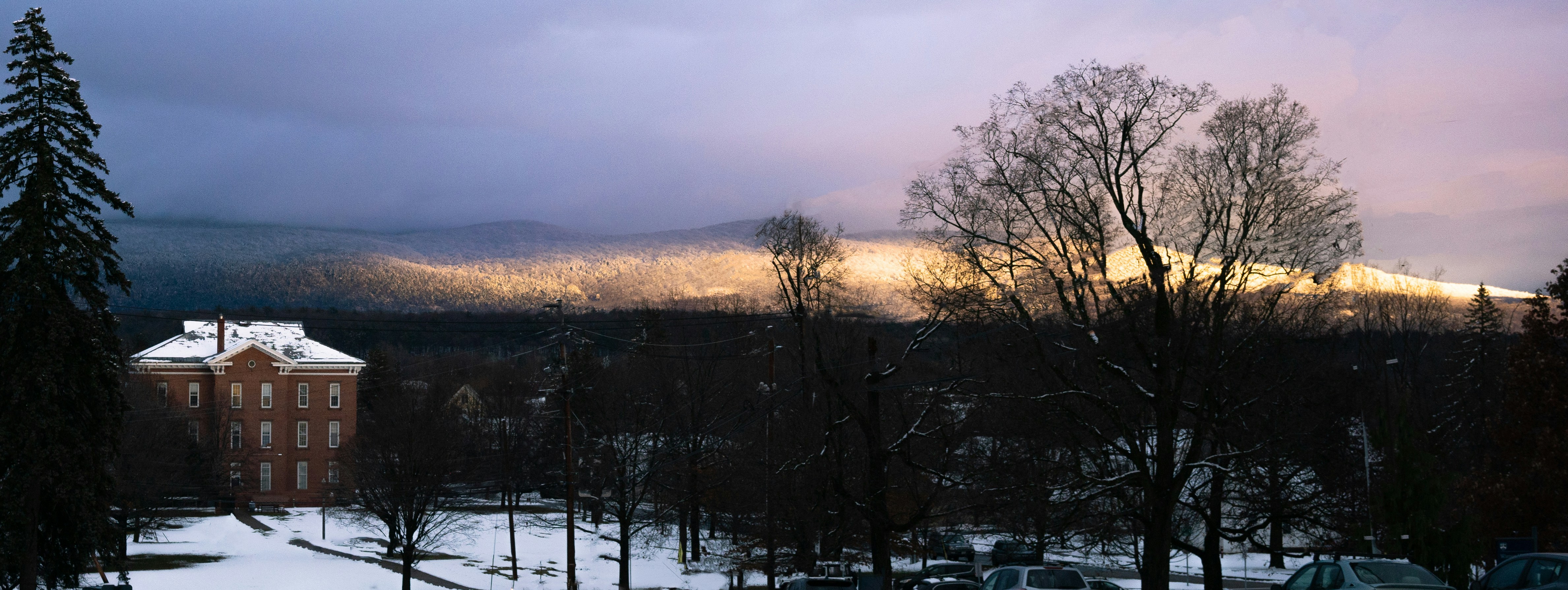 Snowy landscape with a building and bare trees at dusk