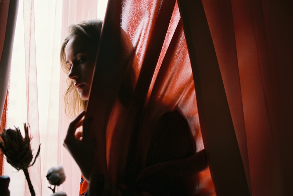 une femme debout devant une fenêtre tenant une rose