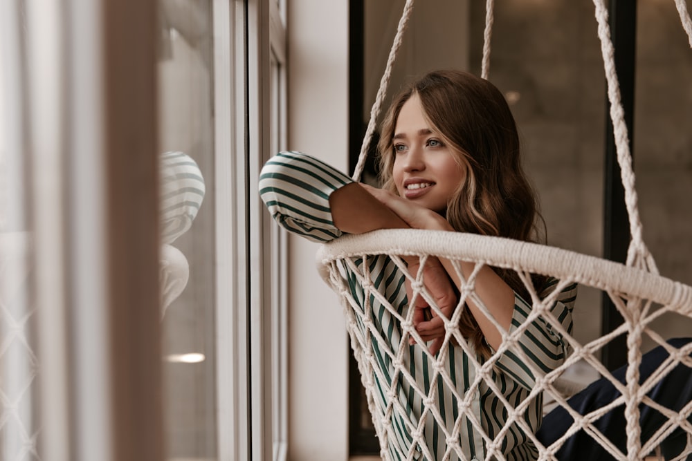 a woman sitting in a hammock looking out the window
