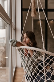 a woman sitting in a hammock looking out a window