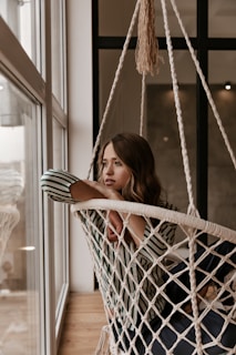 a woman sitting in a hammock looking out a window