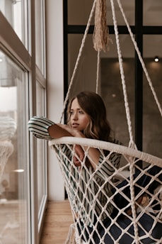 a woman sitting in a hammock looking out a window