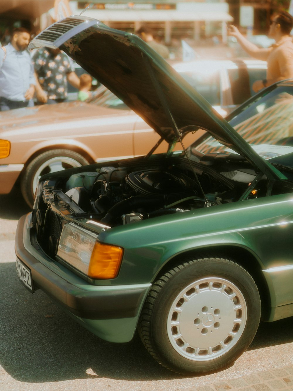 a green car with its hood open in a parking lot