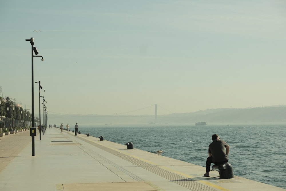 a man sitting on the edge of a pier next to the ocean