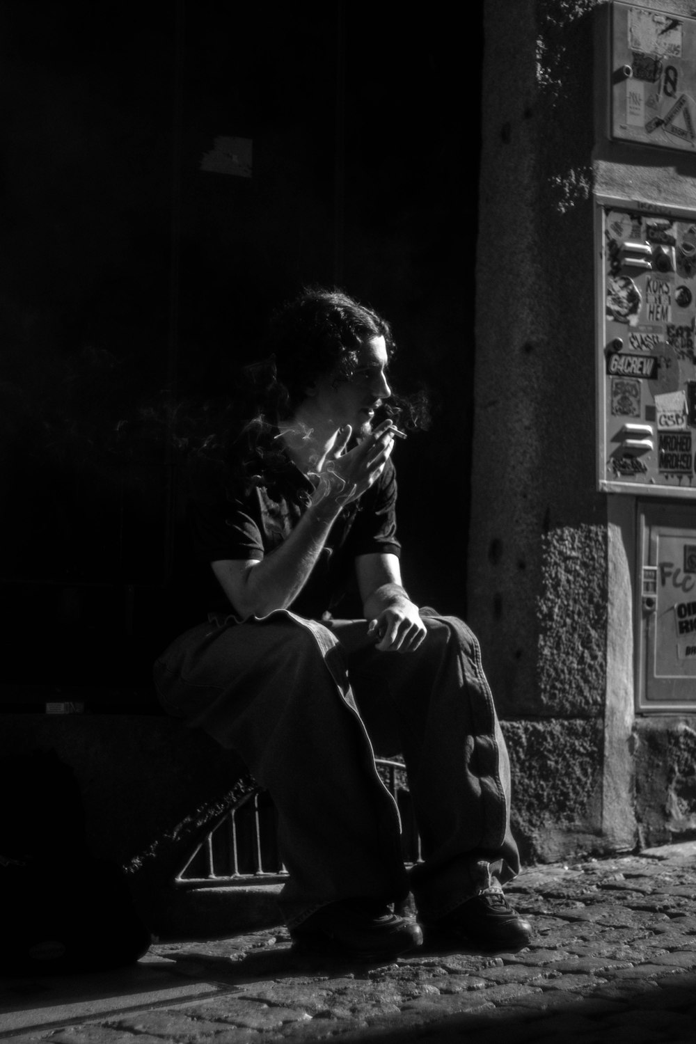 a man sitting on a sidewalk smoking a cigarette
