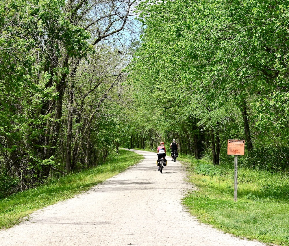 a couple of people riding on the back of a motorcycle down a dirt road