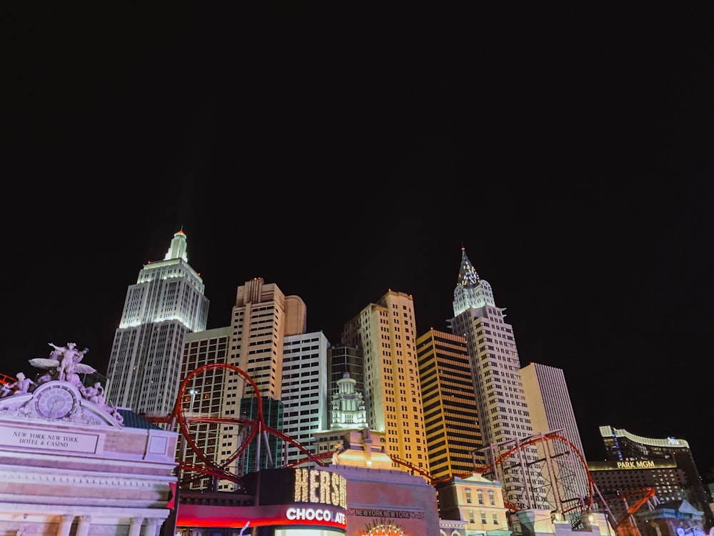 a city at night with tall buildings and a roller coaster