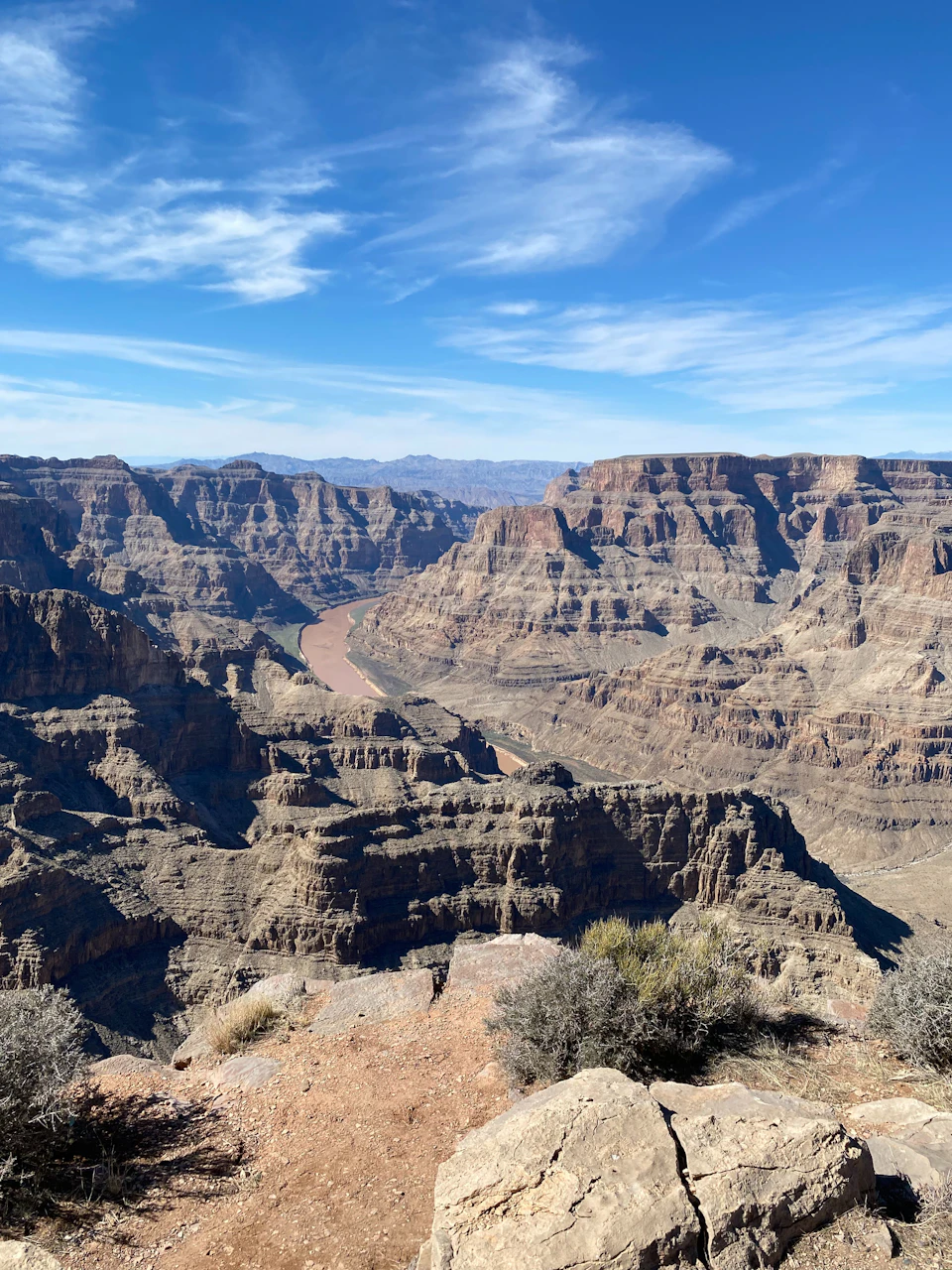 The image depicts a breathtaking view of the Grand Canyon, with its deep red rock layers contrasting against the clear blue sky and light brown mountains in the distance. The canyon is viewed from a high vantage point, offering a panoramic perspective that showcases the vastness and grandeur of this natural wonder. The colors in the photo are vibrant, creating a striking visual effect.