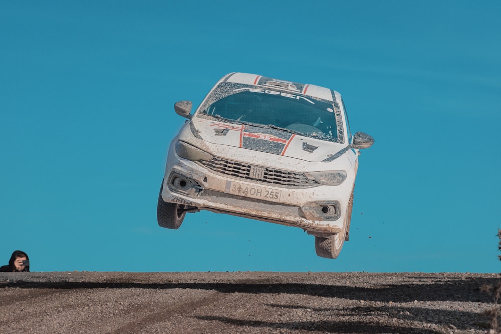 a white car is in the air above a dirt road