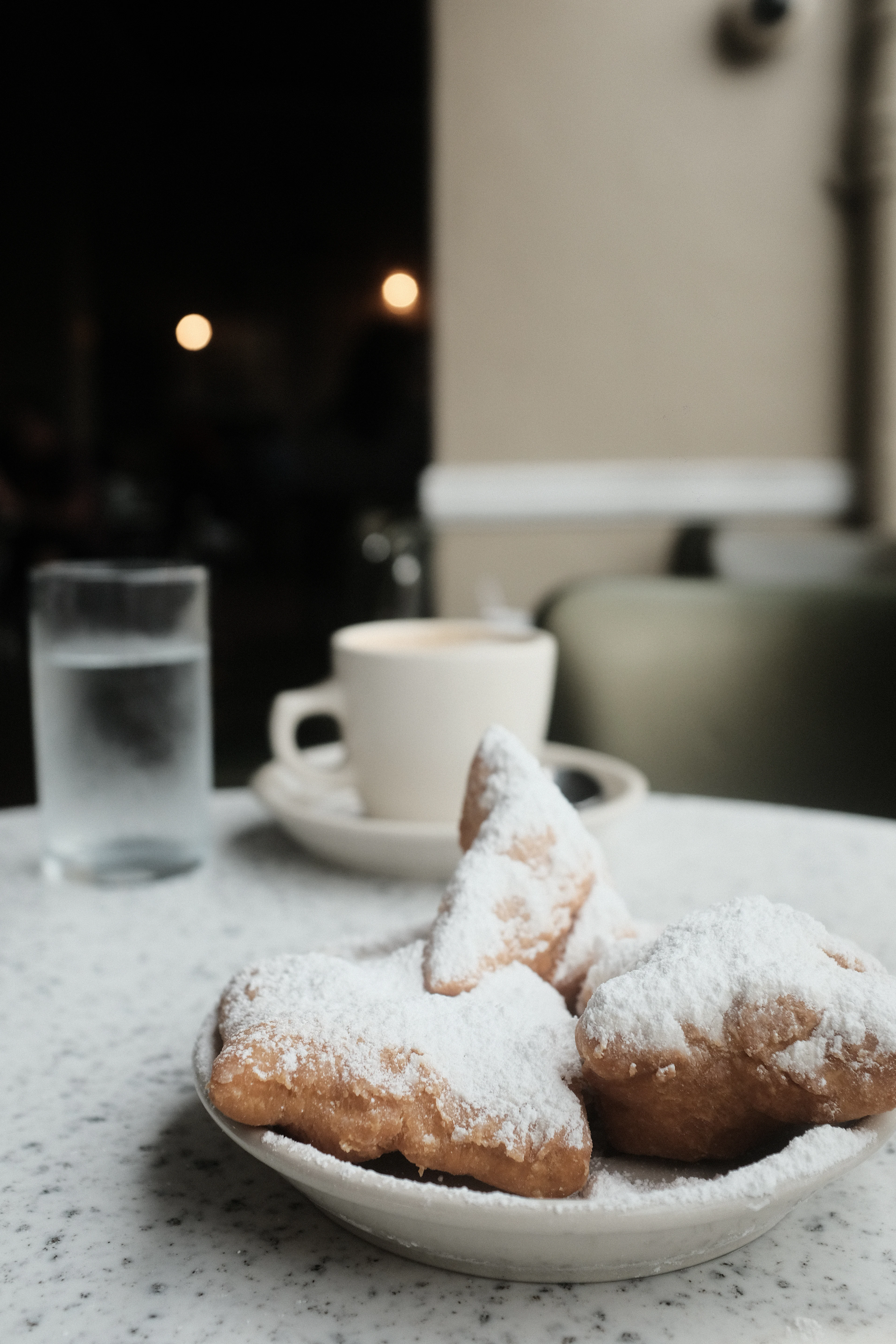 Beignets buried in powdered sugar with a cafe au lait and the customary glass of water, the classic New Orleans Cafe du Monde order
