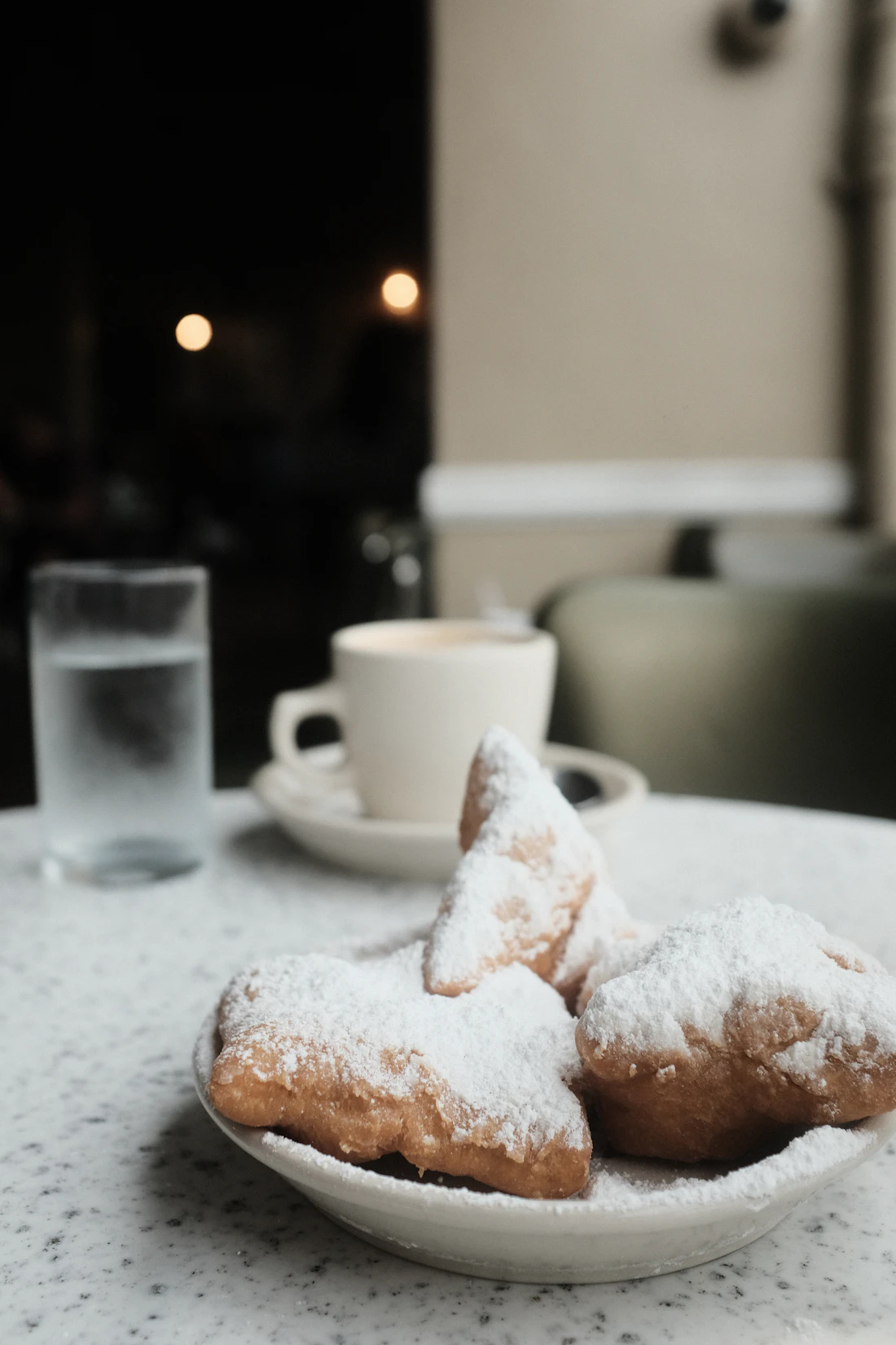 Three beignets covered in powdered sugar beside a cup of cafe au lait