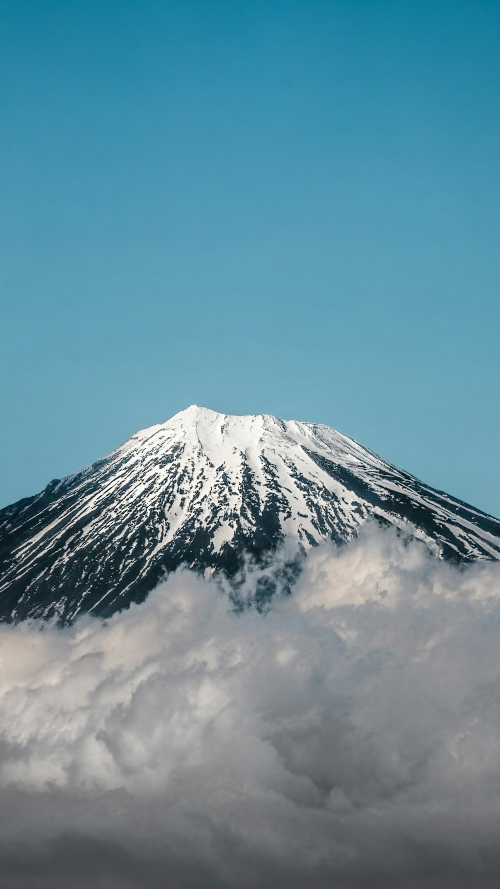 a mountain covered in snow and clouds under a blue sky