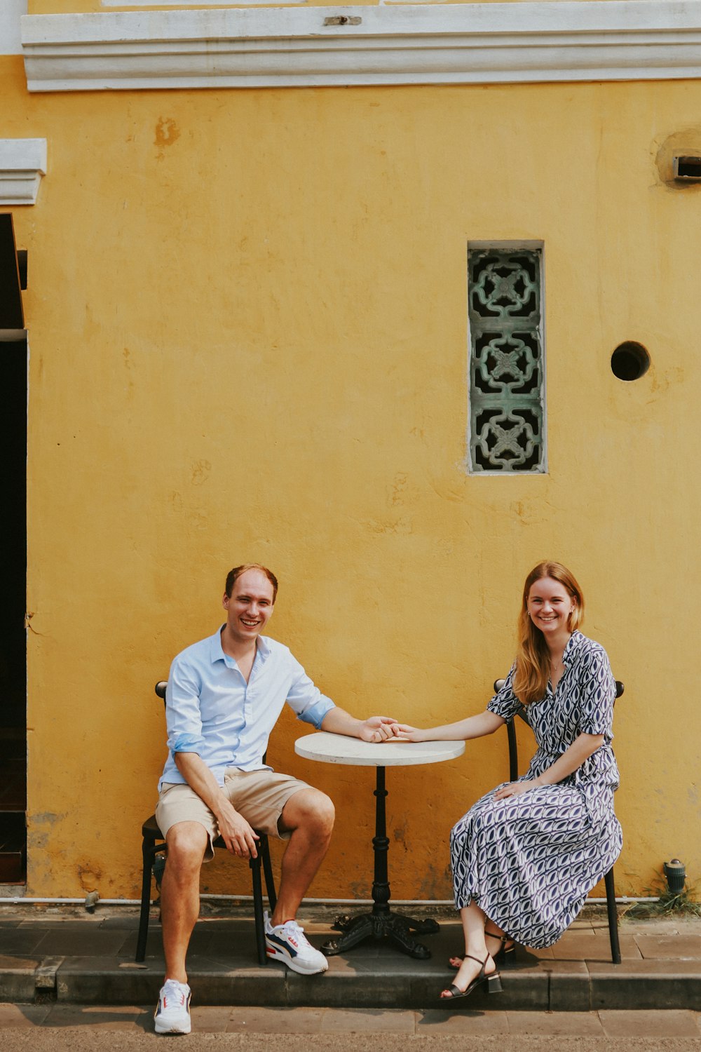 a man and a woman sitting on a bench in front of a yellow building