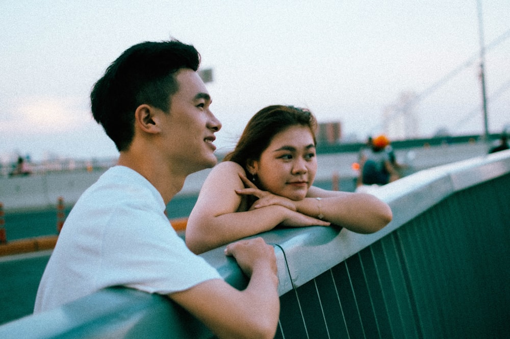 a man and a woman leaning against a fence