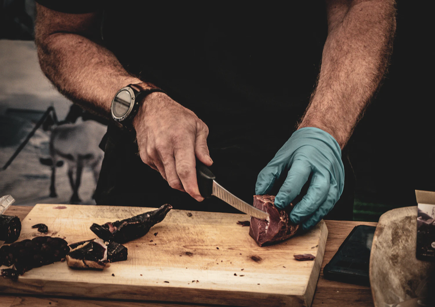 Two hands slicing smoked beef thin across the grain on a wooden board