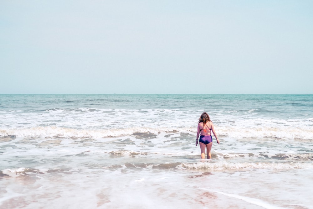 a woman in a bikini walking into the ocean