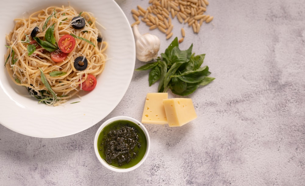 a bowl of pasta with olives, tomatoes, and spinach