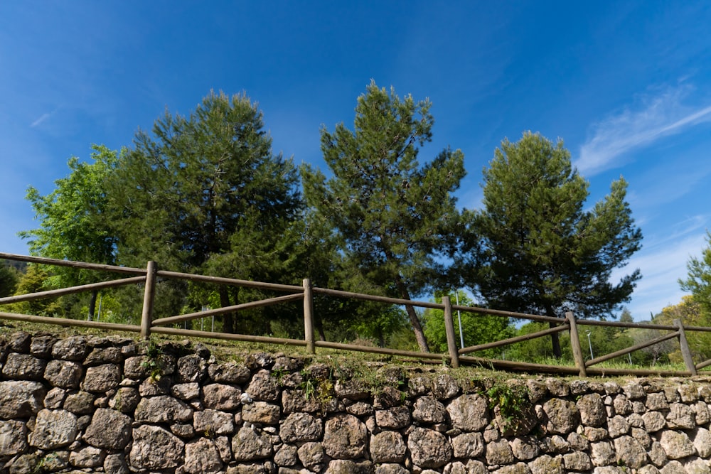 a stone wall with a wooden fence and trees in the background