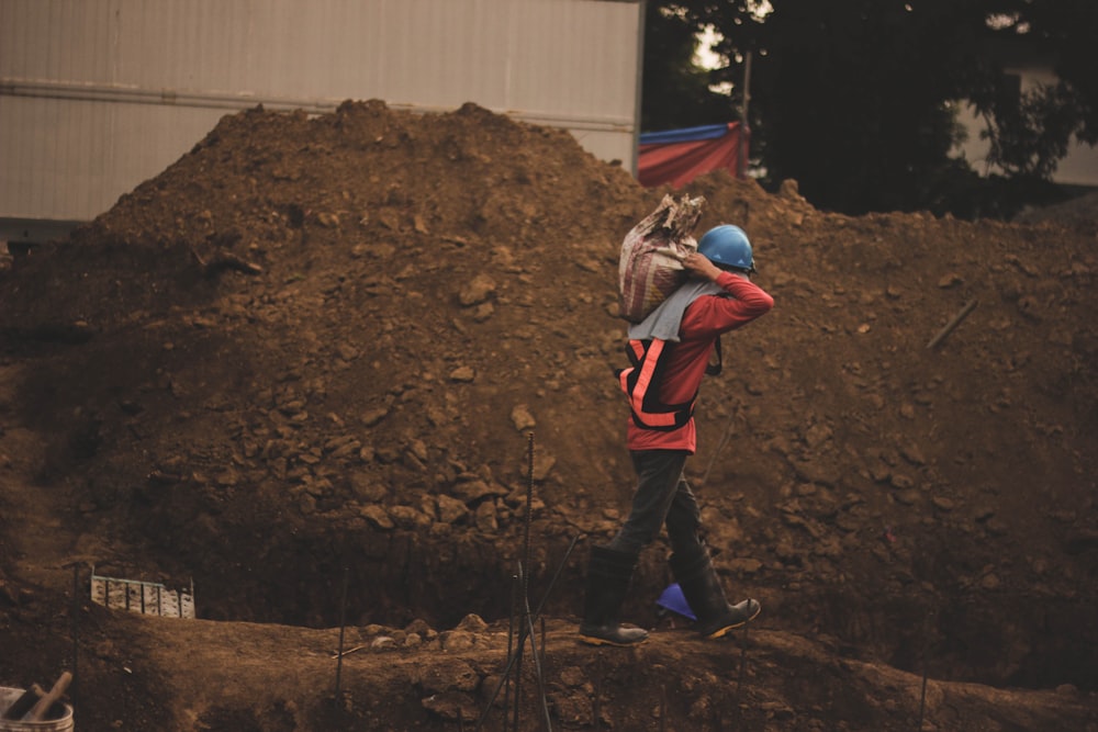 a man carrying a large pile of dirt on top of a dirt field