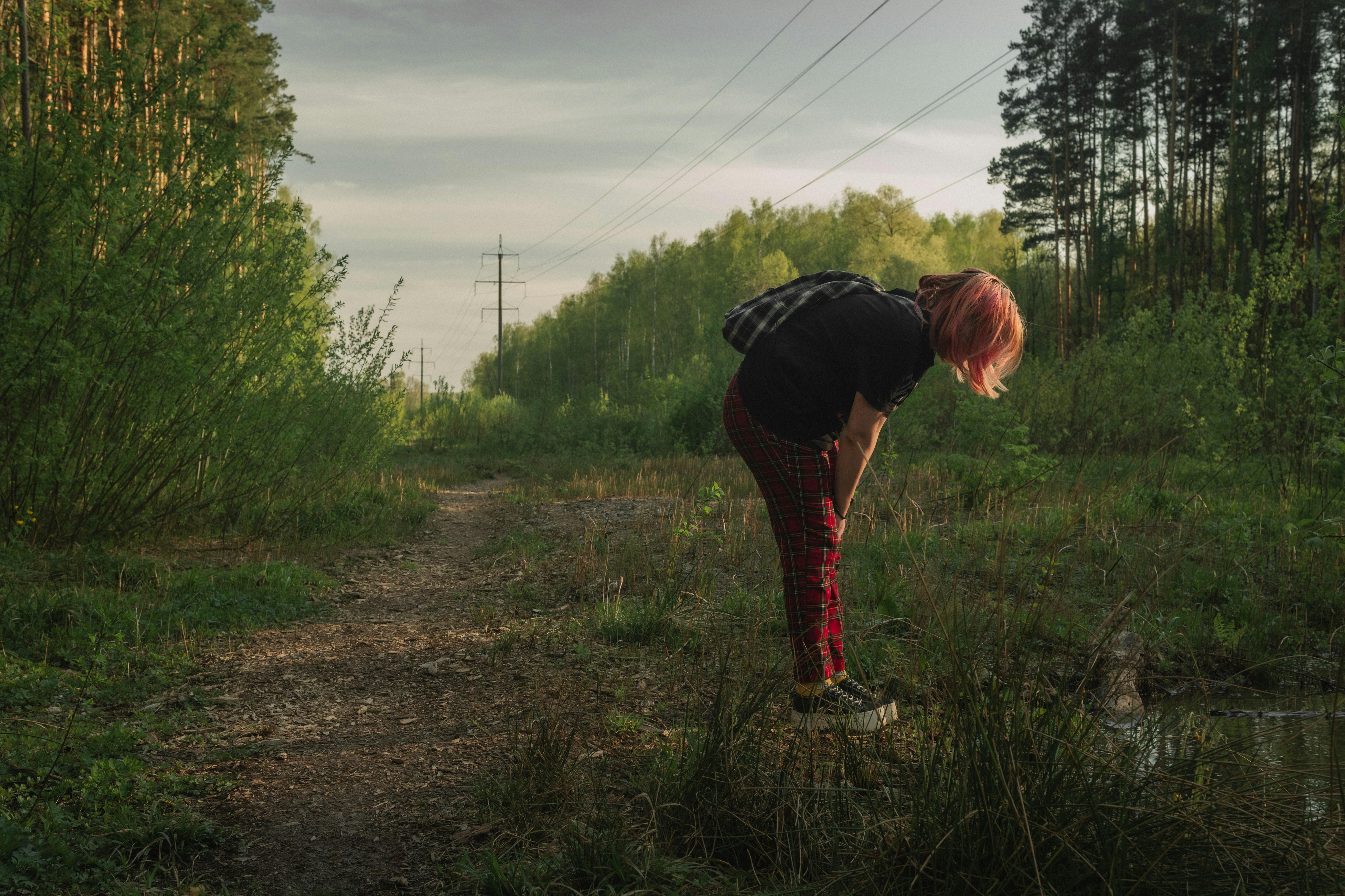 a woman bending over in the grass near a forest