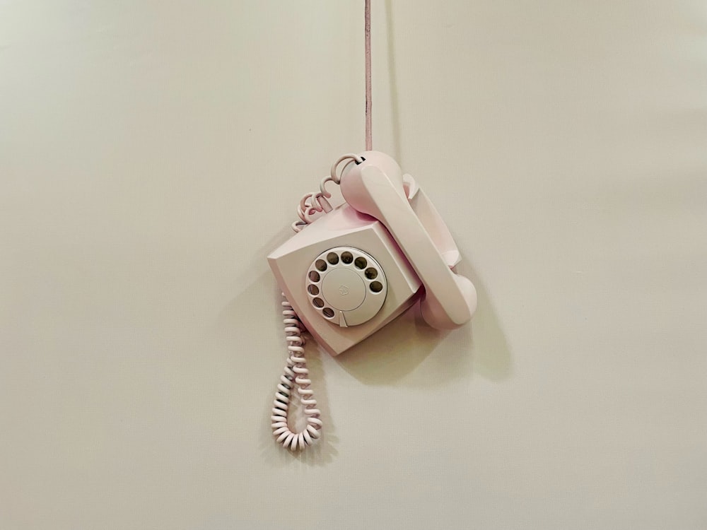 a pink phone hanging from a cord on a wall