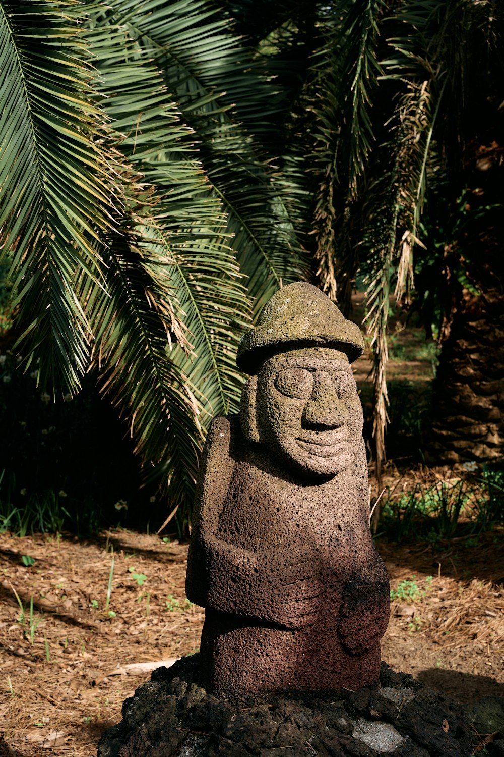 a stone statue of a smiling man in a forest